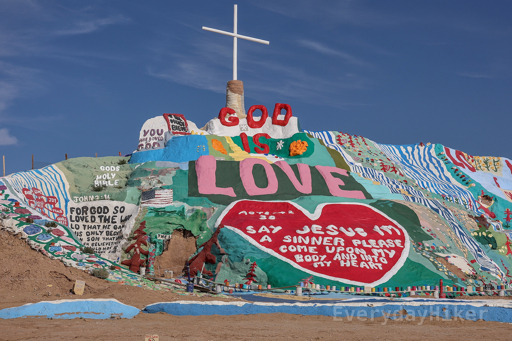 A hillside covered in paint with many religious themed and bible quotes written on it, adorned with a large cross.